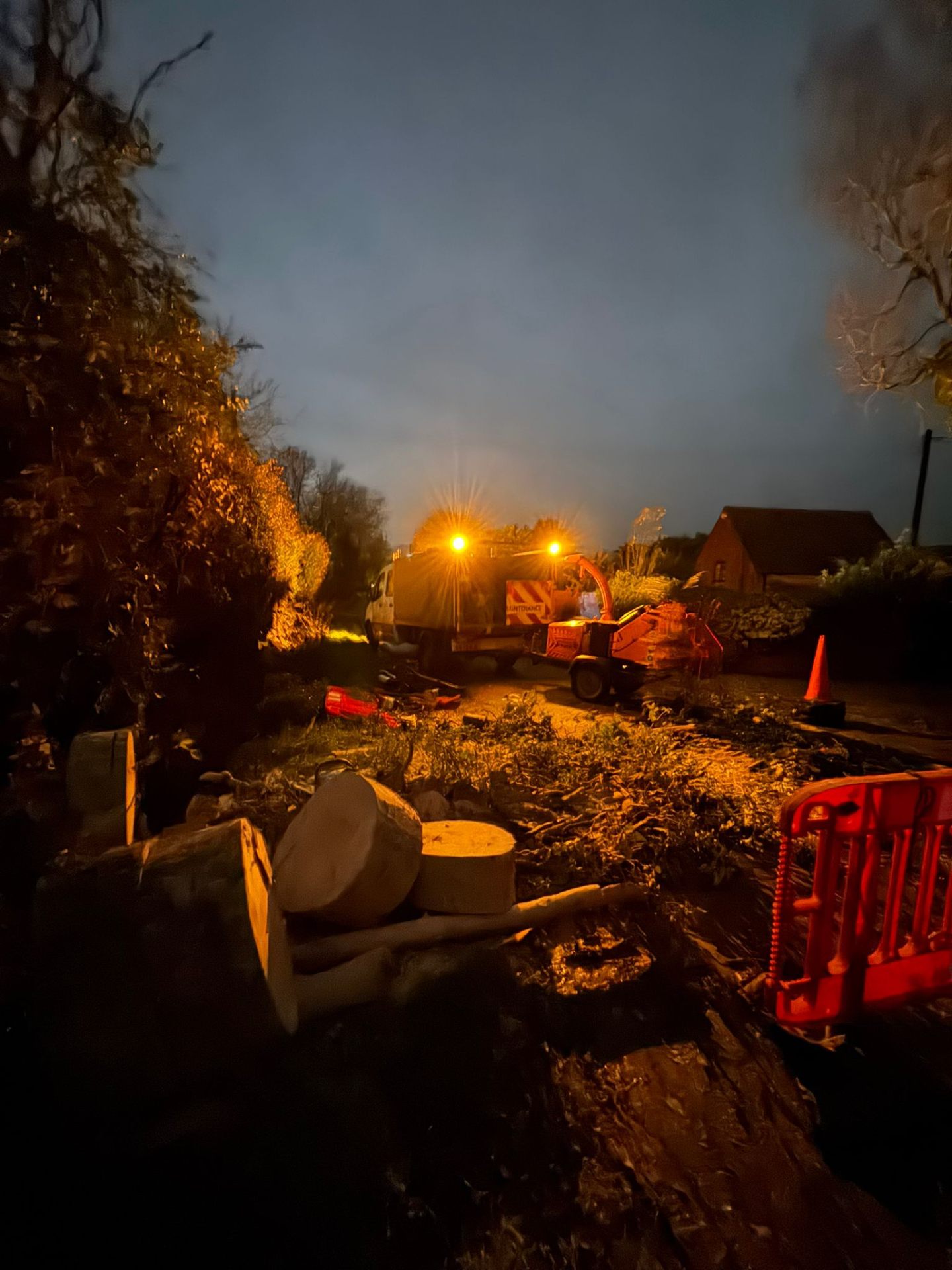 Emergency tree work at night with wood chipper and floodlights clearing storm-damaged trees